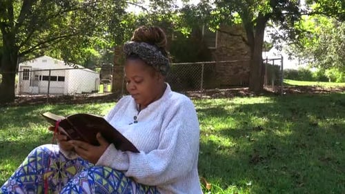 Woman Reading Bible Outdoors on Grassy Lawn