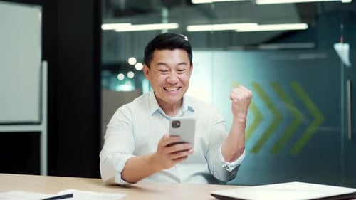 Happy Man Celebrates Success Using Smartphone in Office