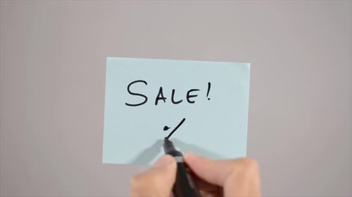 Hand Writes 'SALE!' on Light Blue Note