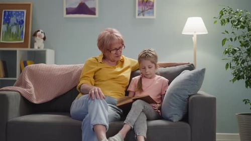 Grandmother and Girl Reading a Book on Couch