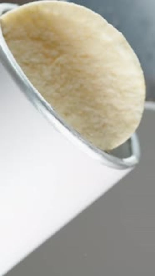 Vertical video. I pour saddle-shaped corn chips from a tall can onto the glass table. Slow motion.