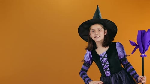 Cheerful Young Witch with Broom Appearing from Corner and Waving on Orange