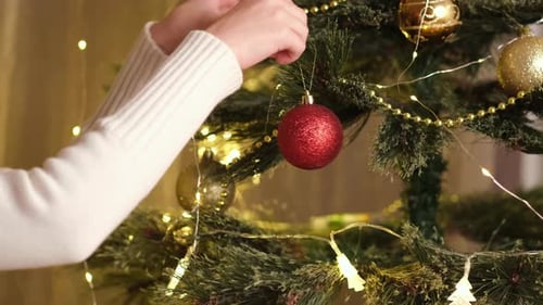 Close Up Kid Hands Decorating Christmas Tree with Balls Near Festive Lights