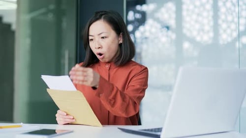 Sad asian woman reading letter with bad news sitting at workplace in modern office. Disappointed
