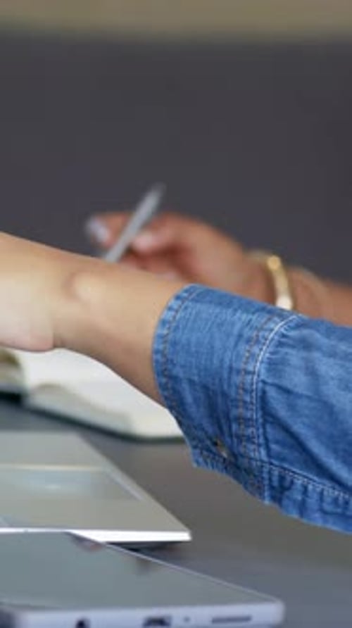 Pointing denim-sleeved forearm tapping laptop trackpad on office table, with notebook and pen