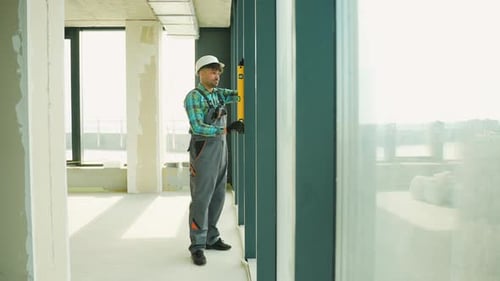 Construction Worker Checking Vertical Alignment of Window Frame with Spirit Level
