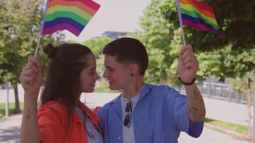 Young Couple Embraces While Holding Rainbow Flags