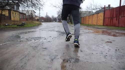 Beine eines jungen Sportlers, der an einem Regentag auf einem ländlichen Pfad läuft Männliche Füße eines sportlichen Läufers beim Joggen