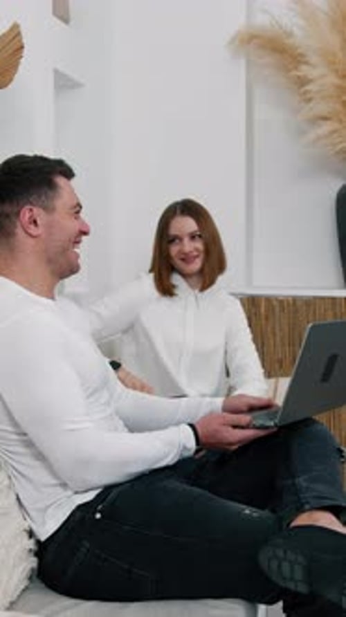Happy relaxed man holding a laptop on his knee and showing it to a lady.