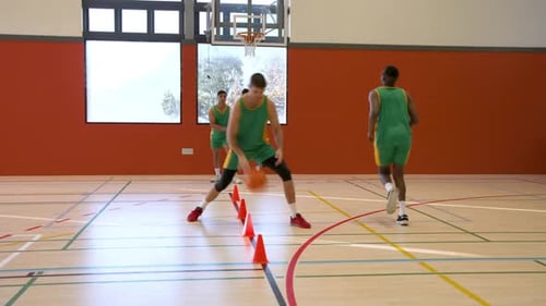 Basketball players practicing dribbling skills in gym with orange cones