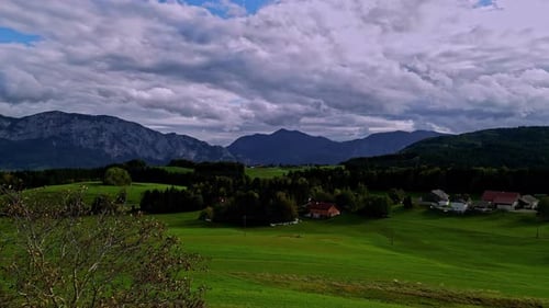 Aerial drone forward moving shot over green grasslands at the foothills of a mountain range on a clo