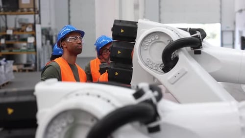 Ein multiethnisches Team von Ingenieuren, die Sicherheitswesten und Helme tragen, analysiert einen Roboterarm in einer Technologie