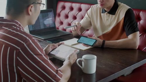 Male Traders Talking about Financial Charts with Gadgets at Table