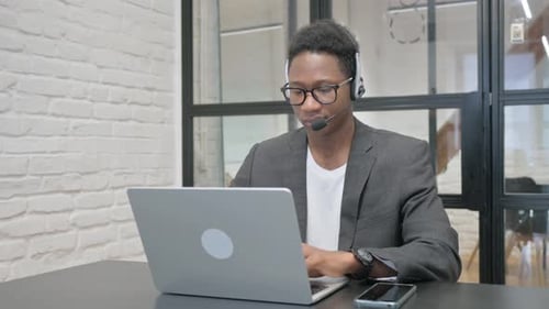 Focused Young Adult Male Working at Laptop with Headset