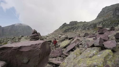 Low angle static shot of Male Hiker with trekking poles and backpack hiking between large rocks in t