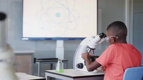 In school, boy using microscope and examining sample in science classroom