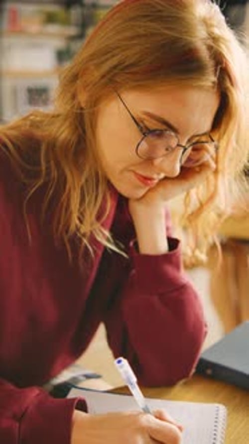 Woman Writing in Notebook Using Laptop in Classroom