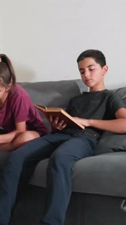 Teens Studying on Couch As Boy Flips Book and Girl Writes Notes Attentively