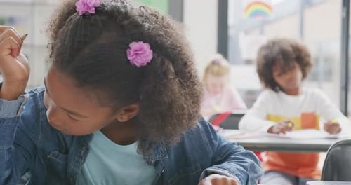 Video of portrait of happy biracial schoolgirl sitting at desk working in school class