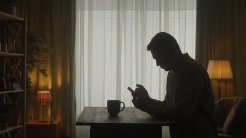 Un homme debout à une table avec un téléphone à la main boit du café Un homme tape un message regarde