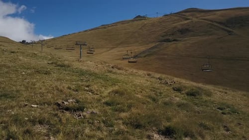 Drone flying low on green mountain meadows with empty stopped ski lift during summer, French