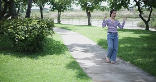 Cheerful woman leisurely strolls along a concrete path and listens to music on her wireless headphon