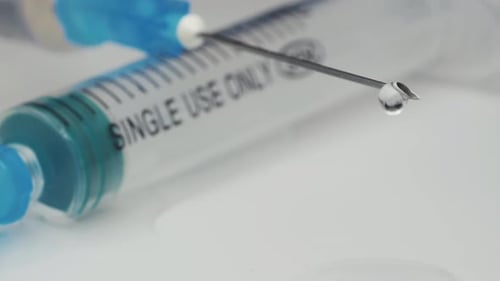 A medical syringe with a vaccine dripping from a needle. Reflection in a drop. Close-up.