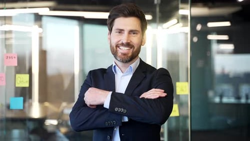 Confident businessman stands with arms crossed in modern office. Wearing a suit,