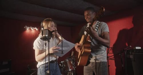 Guy and Woman Record Acoustic Song in Semidark Studio