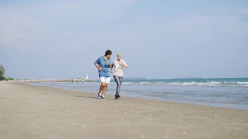 4K Asian senior couple jogging exercise together on the beach in summer morning.
