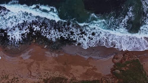 Waves crash on rocky shore during bright daylight hours in coastal area