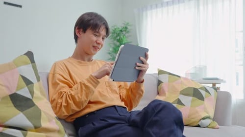 Young Adult Uses Tablet on Couch at Home