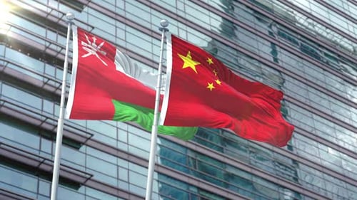 Oman and China Flags Waving in Front of Modern Building