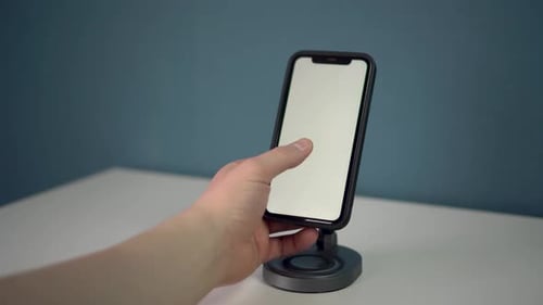The Smartphone is on a Wireless Charging Pad and Shows a White Screen The Man Swipes and Taps Twice