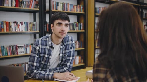 Young Man Engaged in a Thoughtful Conversation with a Woman in a Cozy Library Setting During the Day