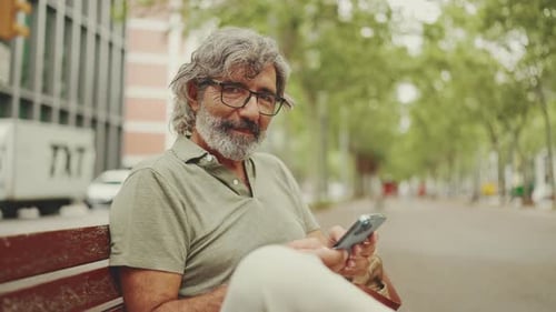 Man Sitting on Bench Using Phone and Smiling