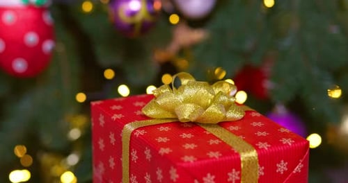 A Red Box with Golden Ribbon Rotates Against Background of Christmas Tree