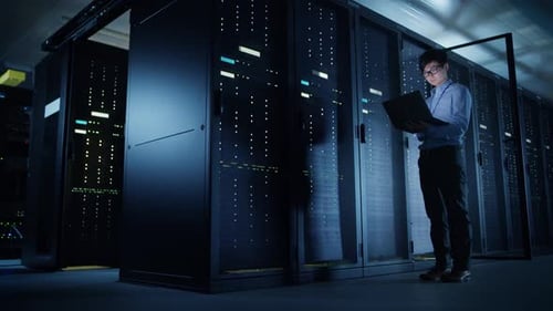 In Data Center: Male IT Technician Running Maintenance Programme on a Laptop, Controls Operational