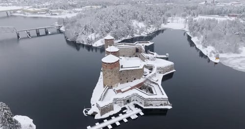 Drone rising around the snowy Olavinlinna castle, cloudy, winter day in Finland