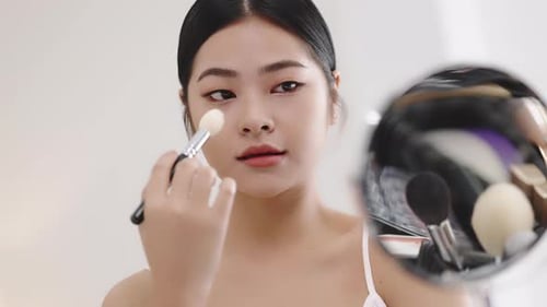 Slow motion shot Close up beauty young pan Asian woman looking at a mirror and applying cosmetics.