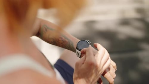 Redhead Female Athlete Checks Smart Watch in Outdoor Gym Monitors Health Stats with Tech Wearable