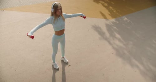Young Woman with Athletic Body Has Workout in Park Outdoors Lifting Dumbbells