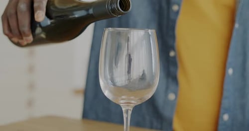 Nahaufnahme einer männlichen Hand, die Rotwein ins Glas gießt, drinnen in der Küche zu Hause