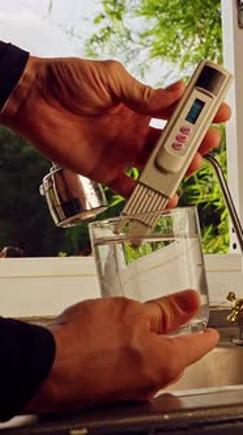 Vue à la première personne des mains testant l'eau potable avec un compteur de qualité numérique indiquant vingt-deux ppm