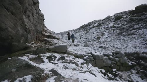 Two people hiking down a frozen, snowy ravine and over rocks in winter.