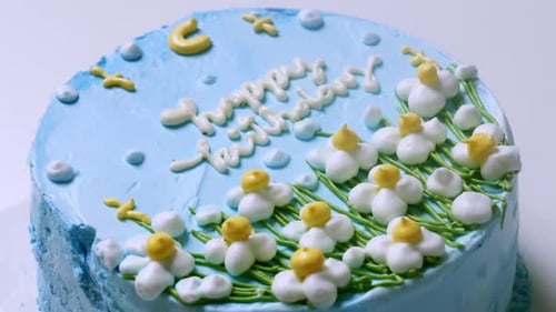 Zooming in of a close-up shot of a blue frosted birthday cake, decorated with small white flowers wi