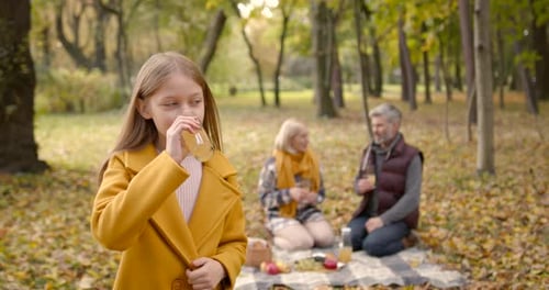 Child Drinks Juice with Grandparents at Autumn Picnic