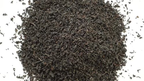 Stapel schwarzen, trockenen Tees auf weißen schwarzen Teeblättern, rotierend auf dem Drehteller, Nahaufnahme, Makro-Ansicht von oben