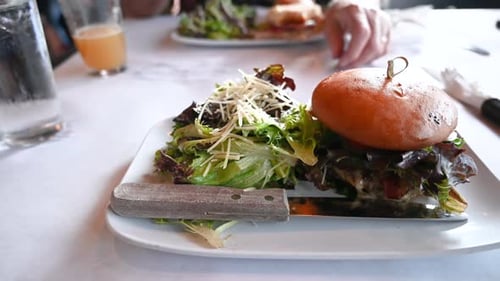 Delicious cheeseburger and side salad with parmesan on white plate on restaurant table.
