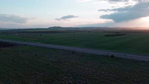 Road with Cars and Trucks on It Passes Through Fields Under a Colored Sky